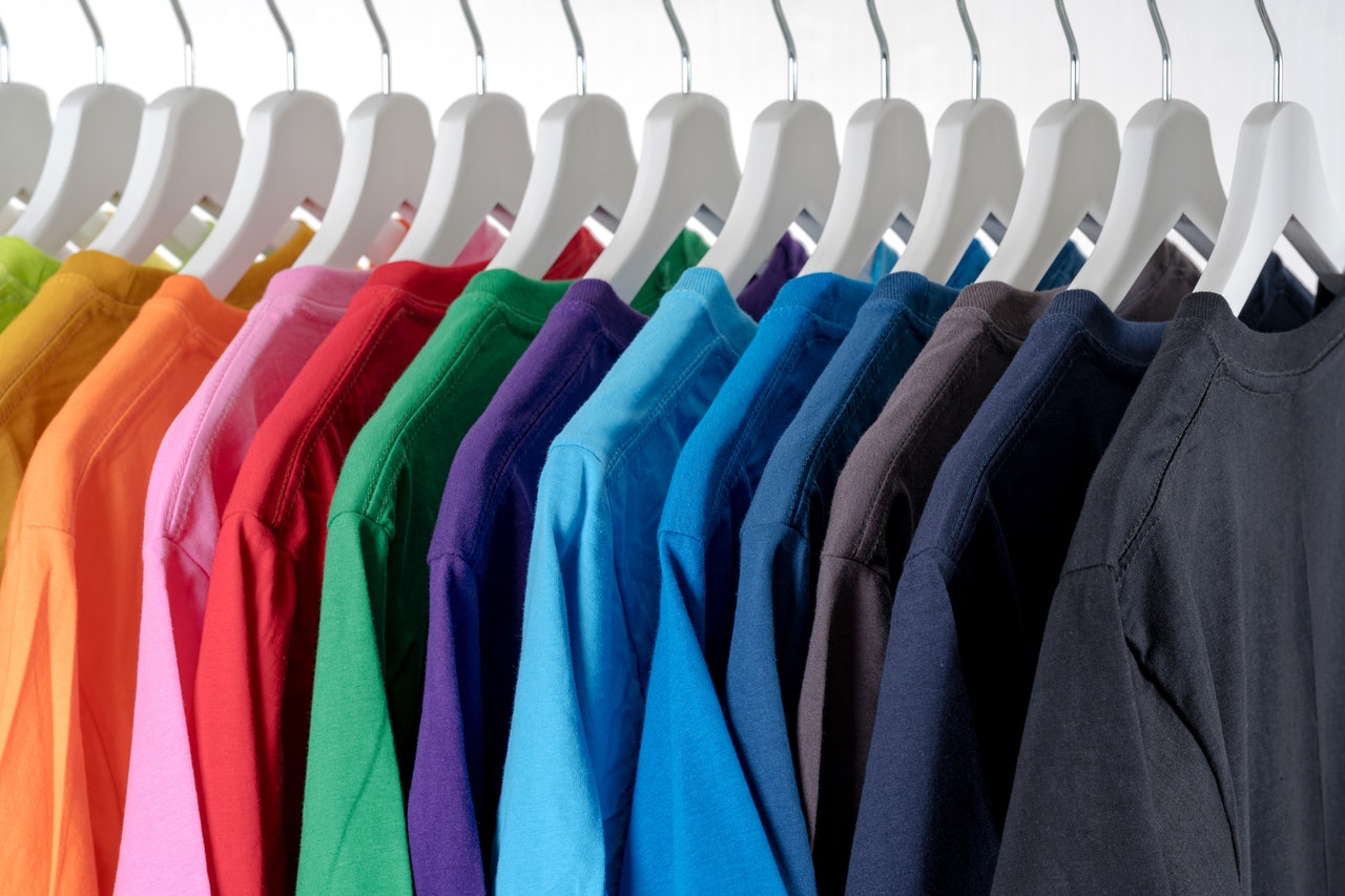 Uz baltiem apģērbu pakaramajiem ir sakārti dažādu krāsu T-krekli, sākot ar gaiši rozā toņiem un beidzot ar tumši zaļiem un ziliem.